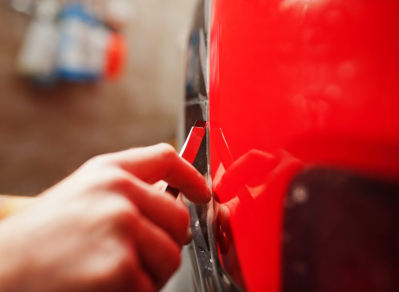 Car service worker put anti gravel film on a red car body at the detailing vehicle workshop. Car protection with special films.