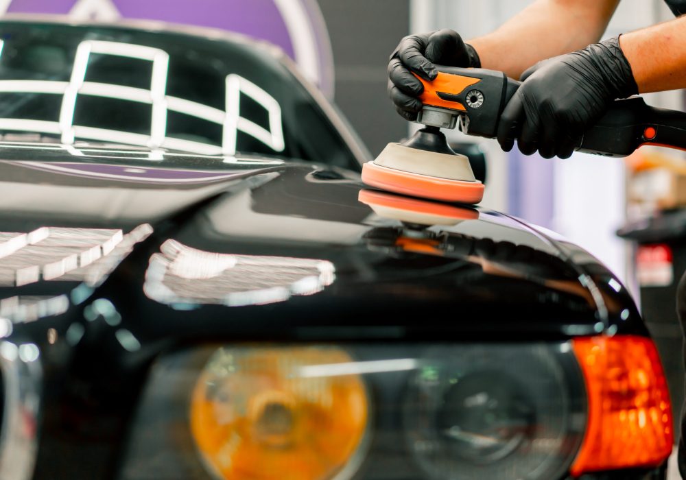 Close-up of a car wash worker using a polishing machine to polish the hood of black luxury car