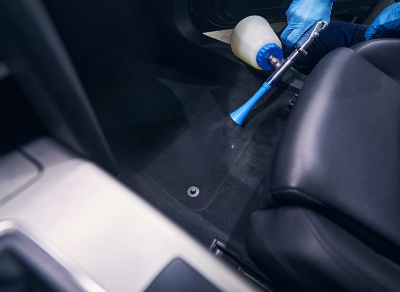 Worker pointing auto detailing air gun at the automobile floor while performing dry cleaning