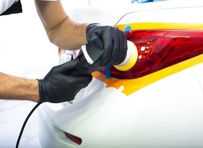 The man is polishing red back lights of a modern white car with polish machine. Close-up view
